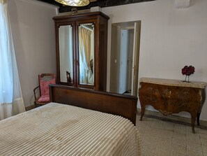A bedroom with a bed, a wooden wardrobe, a mirror, and a small table with a vase. - Spacious Vintage Cottage in Loire Valley: Village Charm, Garden, Pets Welcome (Tavers)