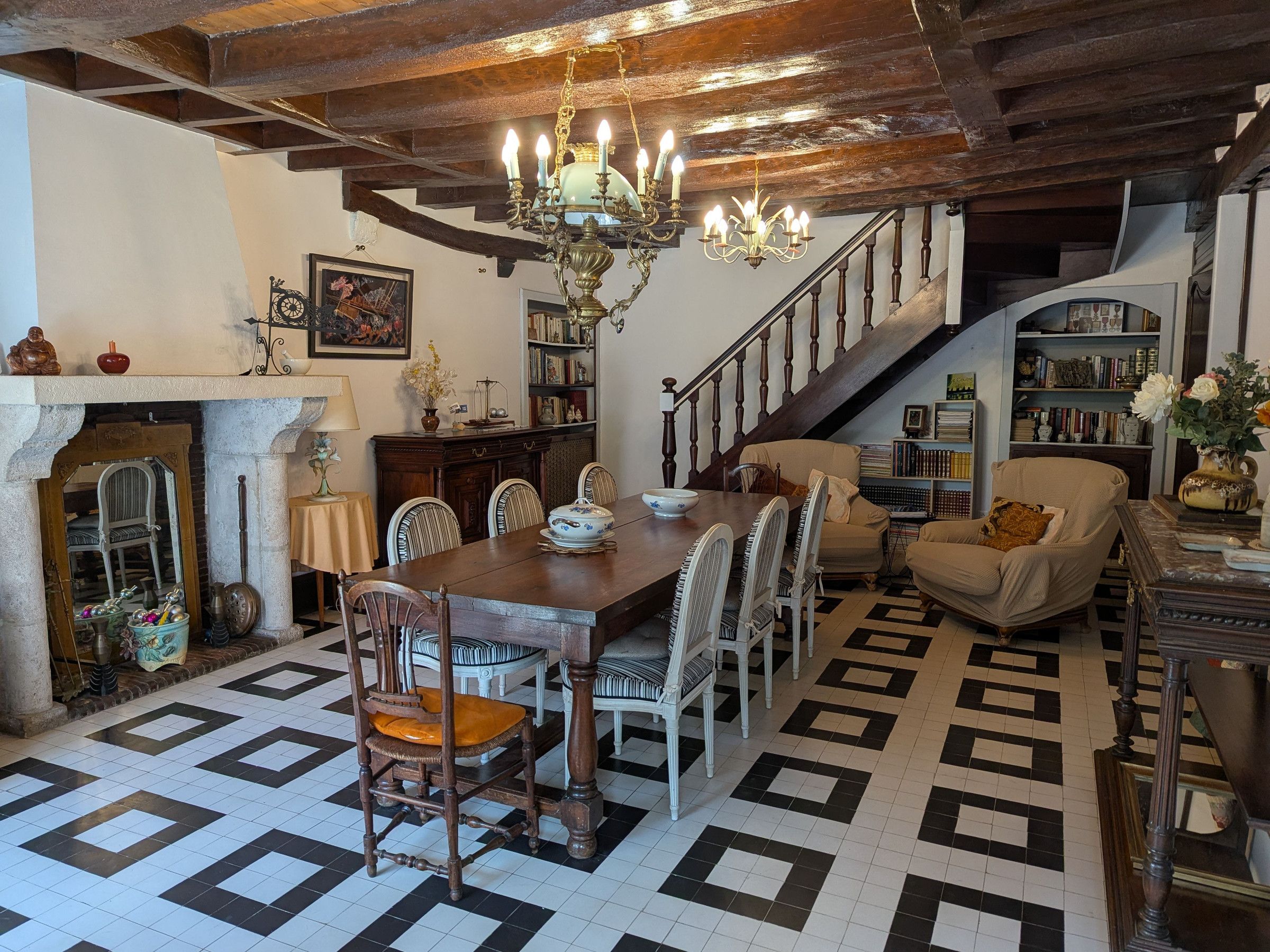 A dining area with a wooden table and chairs, a chandelier, and a staircase leading to a bookshelf.