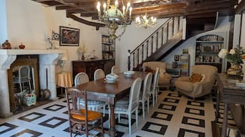 A dining area with a wooden table and chairs, a chandelier, and a staircase leading to a bookshelf.