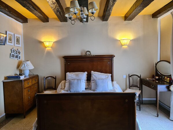 A bedroom with a wooden bed, two wall-mounted lamps, a dresser, a chair, and a mirror.