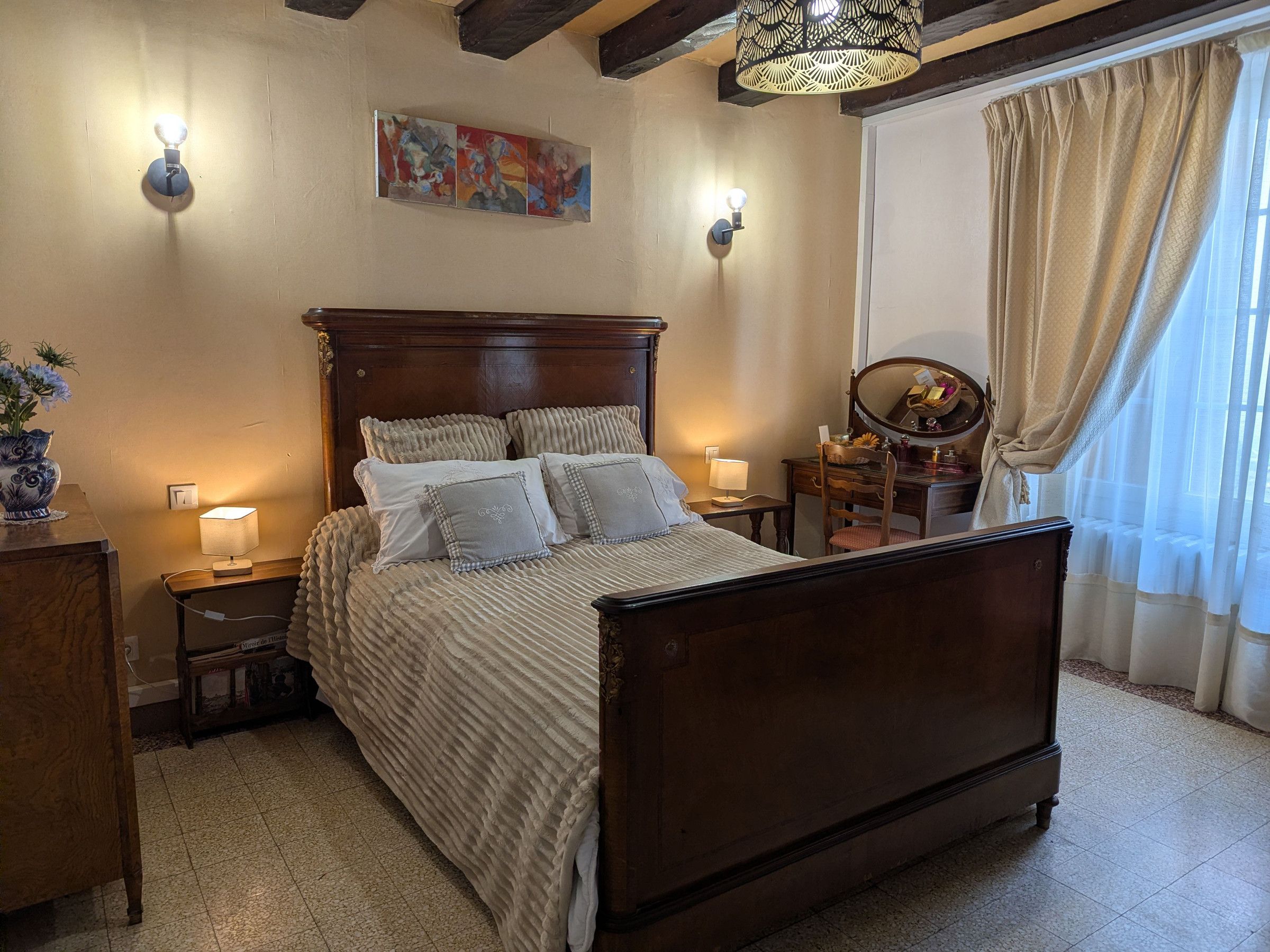 A bedroom with a wooden bed, bedside lamps, a dresser, a mirror, and a painting on the wall.