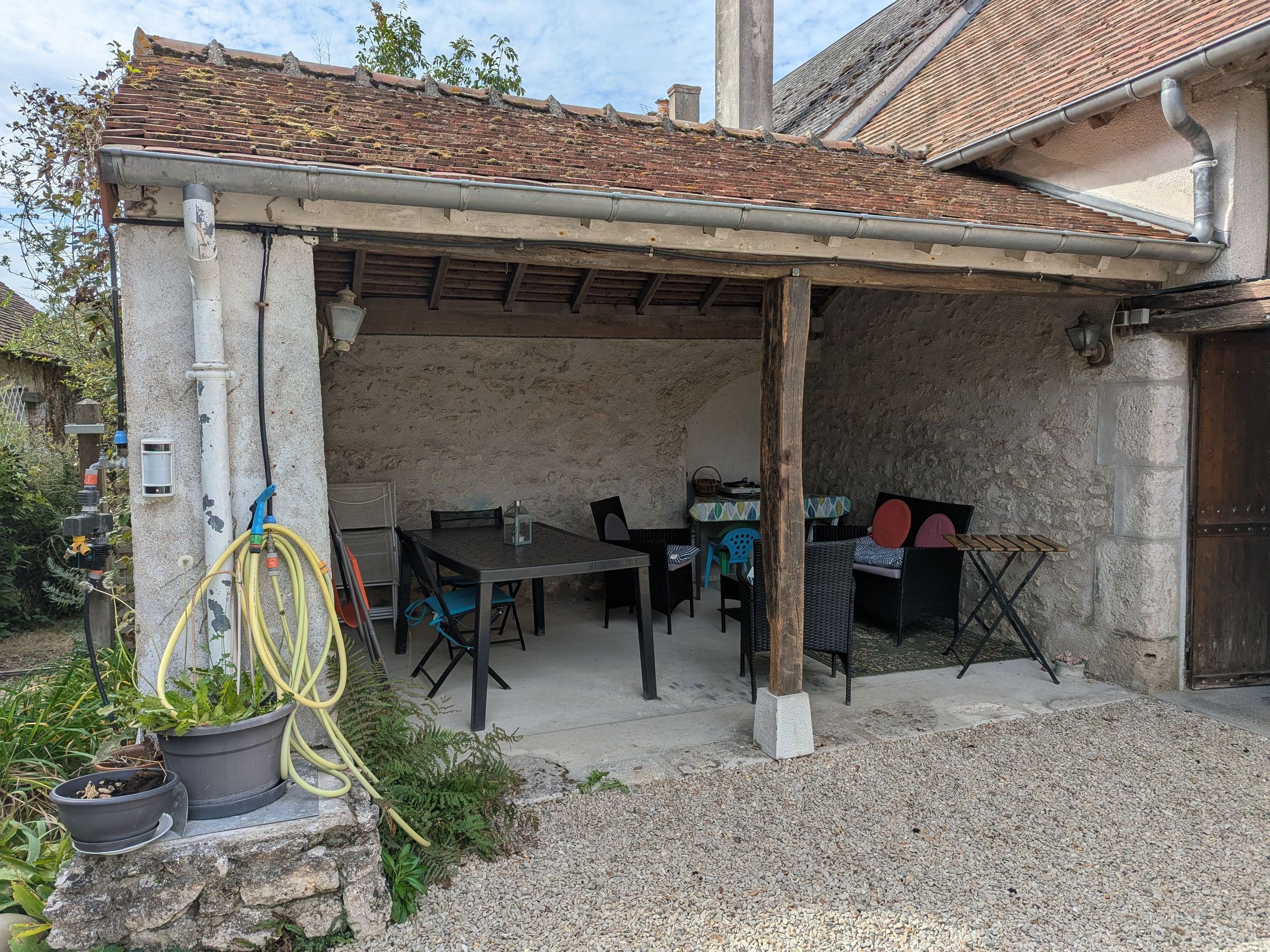 An outdoor patio with a table and chairs, surrounded by stone walls and a tiled roof.