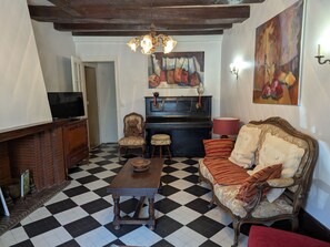 A room with a checkered floor, a piano, a sofa, a television, and a chandelier. - Spacious Vintage Cottage in Loire Valley: Village Charm, Garden, Pets Welcome (Tavers)