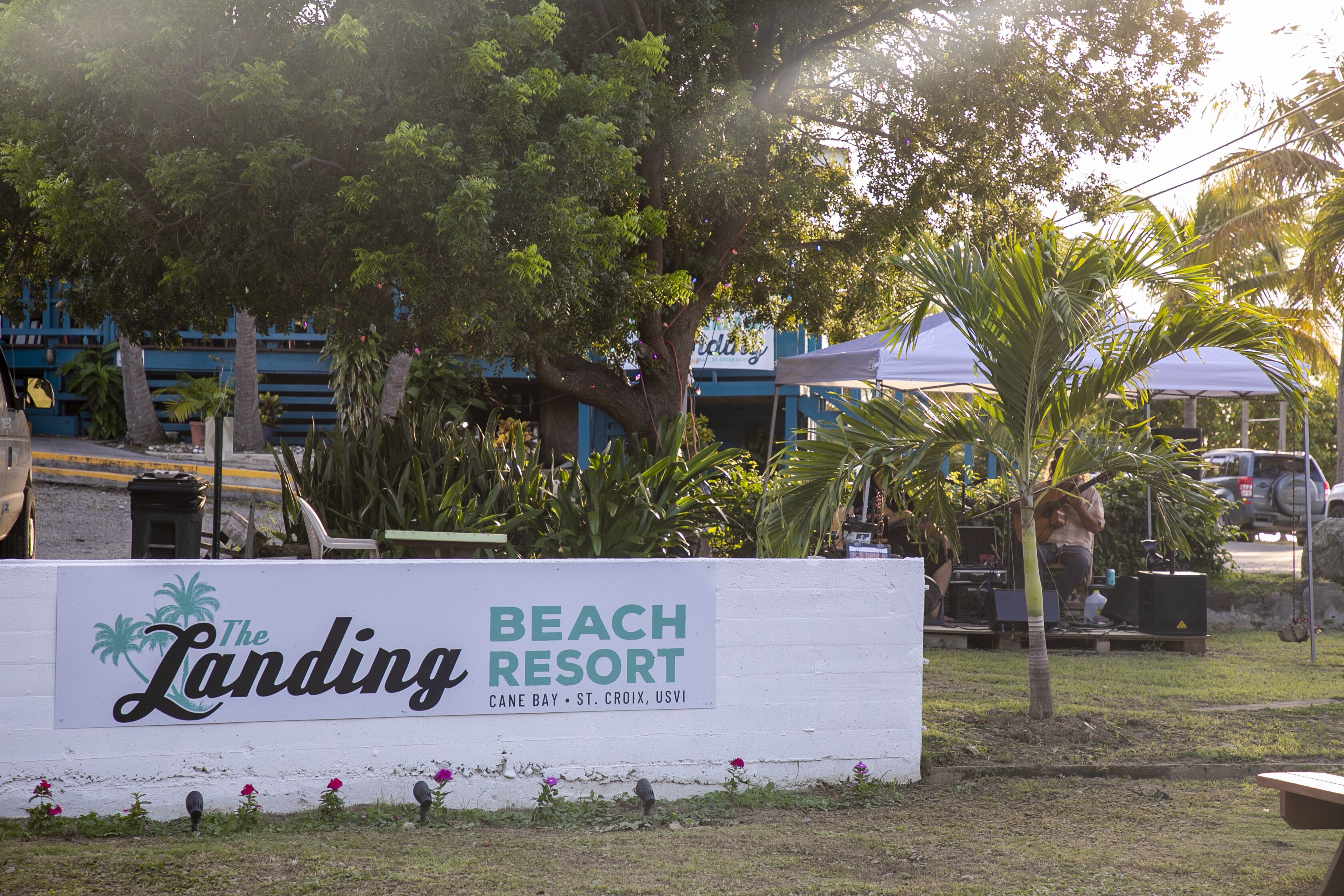 Een bord voor The Landing Beach Resort, met een palmboom en bloemen op de voorgrond.