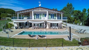 Ein modernes, zweistöckiges Haus mit großem Pool, Außenbereich zum Sitzen und Blick auf die umliegende Grünfläche.
