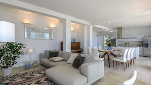 Ein modernes Wohnzimmer mit einer Couch, einem Esstisch mit Stühlen, einem Klavier und einer Küchenzeile mit Kühlschrank.