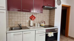 A kitchen with white cabinets, a stainless steel sink, a red kettle, and a stove.