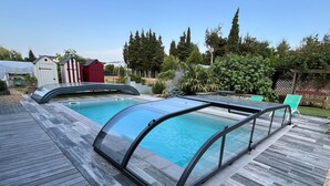 Une piscine dotée d’une enceinte en verre, entourée d’une terrasse en bois et agrémentée de divers éléments de jardin.