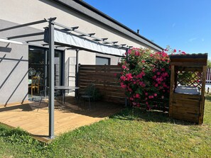 Eine Terrassenfläche mit Tisch und Stühlen, einem Holzzaun und einem Blumenkasten mit rosa Blüten.