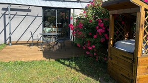 Une terrasse avec une table et des chaises, une plateforme en bois et une structure en bois surmontée d’un matelas.