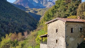 Ein rustikales Steinhaus mit geneigtem Dach, umgeben von üppiger Vegetation und Bergen im Hintergrund.