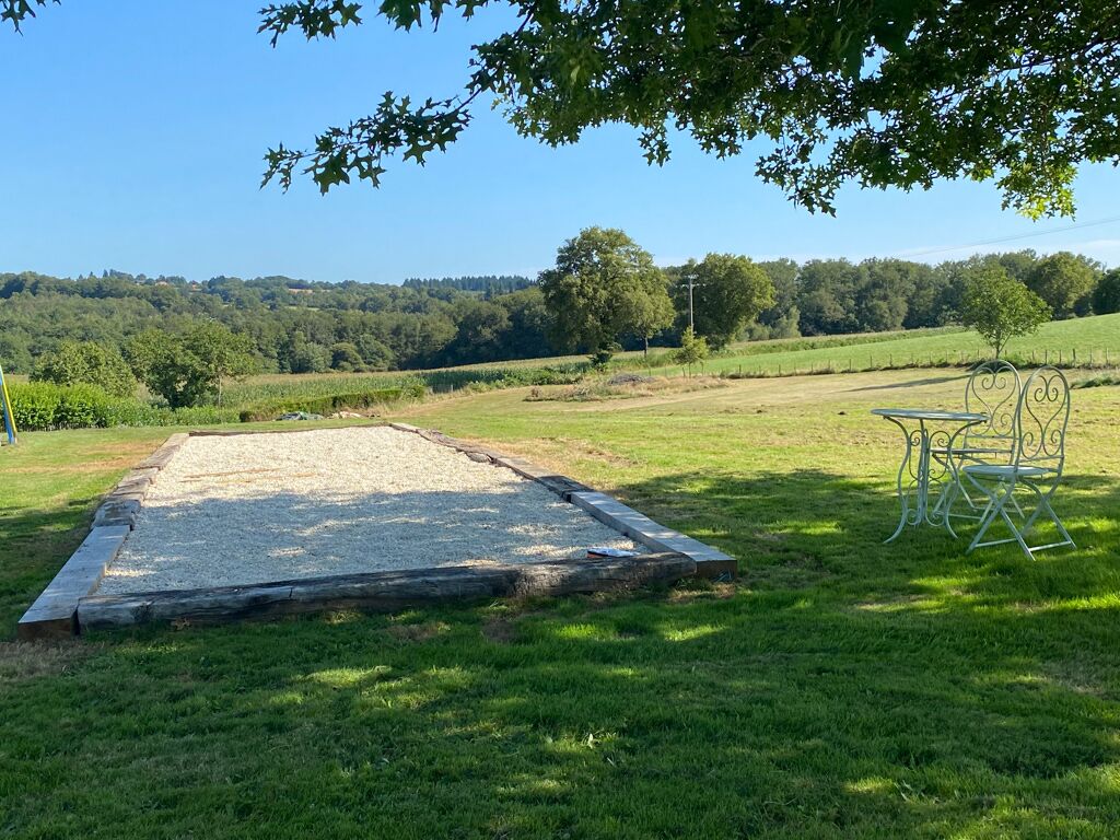 Un espace extérieur avec un bac à sable et des chaises en métal, situé sous un arbre.