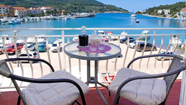 Un balcon avec deux fauteuils confortables, une petite table ronde agrémentée d’un objet décoratif, et une vue sur une marina avec des bateaux et des bâtiments.