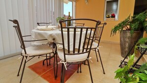 Un coin repas avec une table dressée pour quatre personnes, entourée de chaises, d’une plante en pot et d’une fenêtre ornée de fleurs.