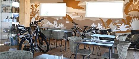 A restaurant with wicker furniture, bicycles, and a mural on the wall.