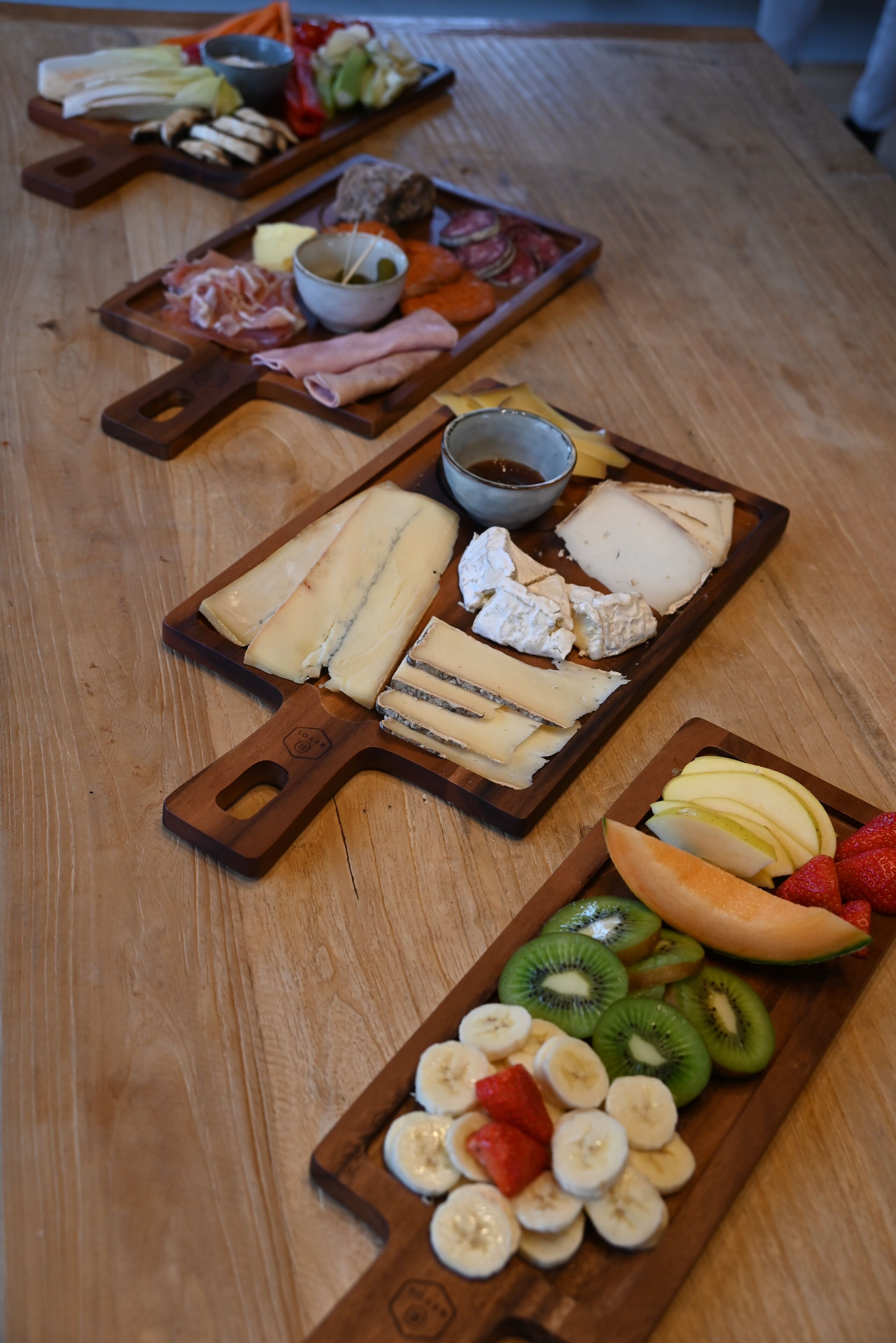 Una mesa de madera con diversas opciones de comida, como quesos, frutas y embutidos.