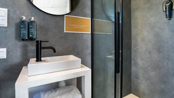 A modern bathroom with a white sink, black faucet, and a glass shower enclosure. There are two bottles of shampoo and a plaque on the wall.