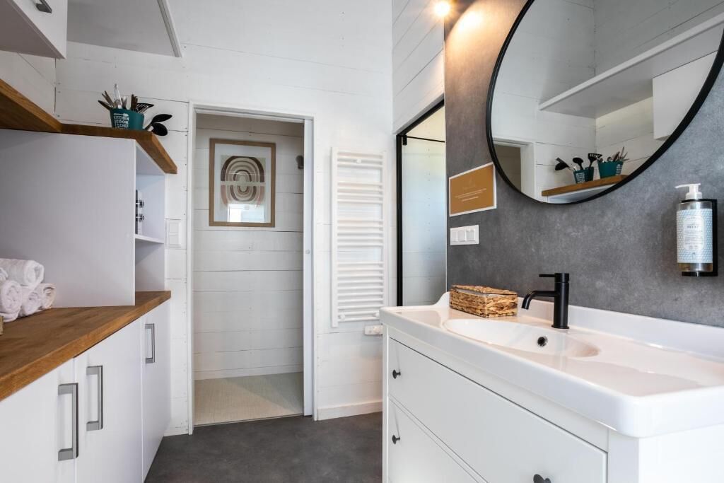 A modern bathroom with a white vanity, a large mirror, and a wooden shelf.