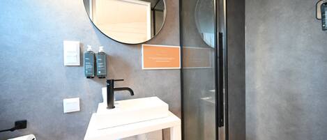 A modern bathroom with a white sink, a round mirror, and a glass shower enclosure.