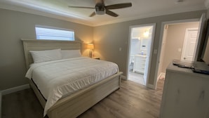 Une chambre à coucher comprenant un lit, un ventilateur de plafond, une table de chevet avec une lampe et une commode.