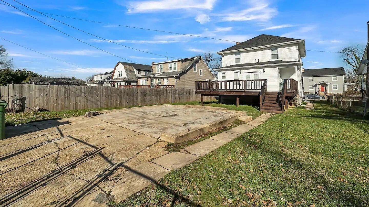 A backyard with a concrete patio, a wooden deck, and a fenced area.