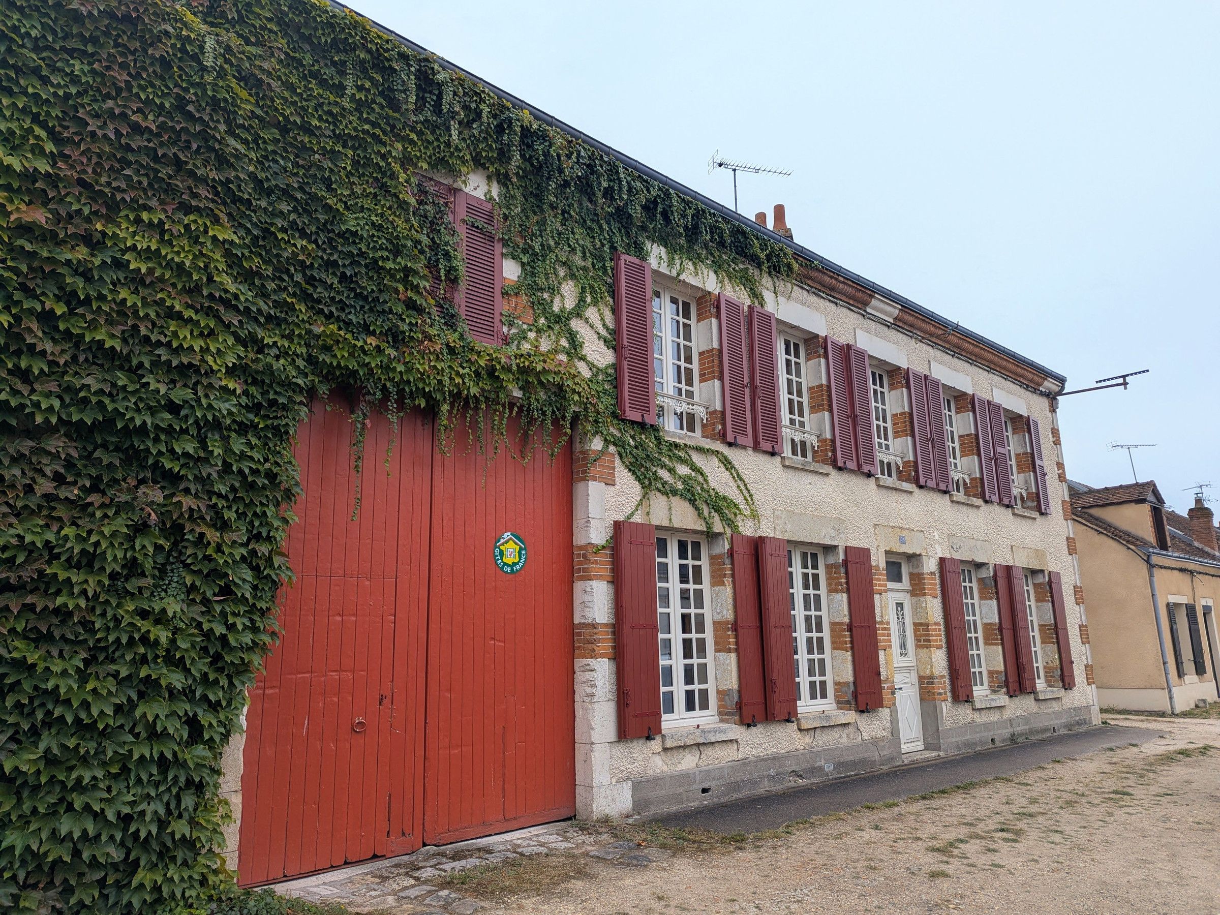 A building with a red garage door, multiple windows with shutters, and a sign indicating a business or service.