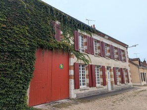 A building with a red garage door, multiple windows with shutters, and a sign indicating a business or service.