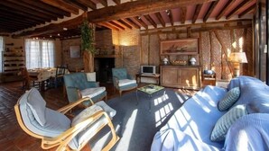 Un salon rustique avec des poutres apparentes, une cheminée et un coin salon confortable avec un canapé et des fauteuils.