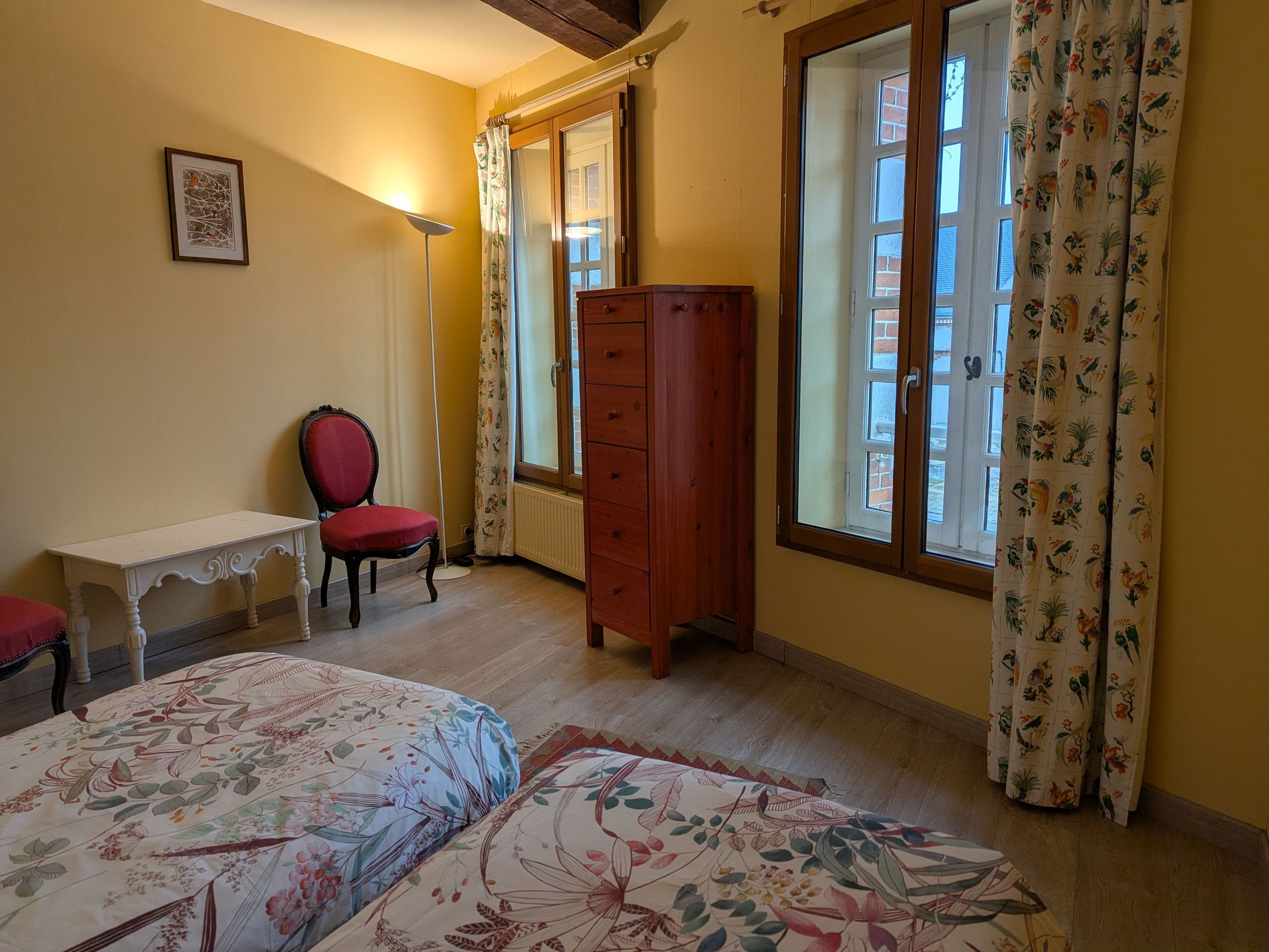 A bedroom with a bed, a chair, a dresser, and a window with curtains.