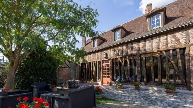 Une cour dotée d’un espace extérieur aménagé avec des sièges, un chemin en pierre et un bâtiment aux grandes fenêtres et aux poutres en bois.