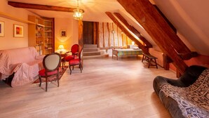 Une pièce mansardée chaleureuse avec un plafond haut, des poutres en bois, un canapé, un fauteuil, une petite table et un lit.