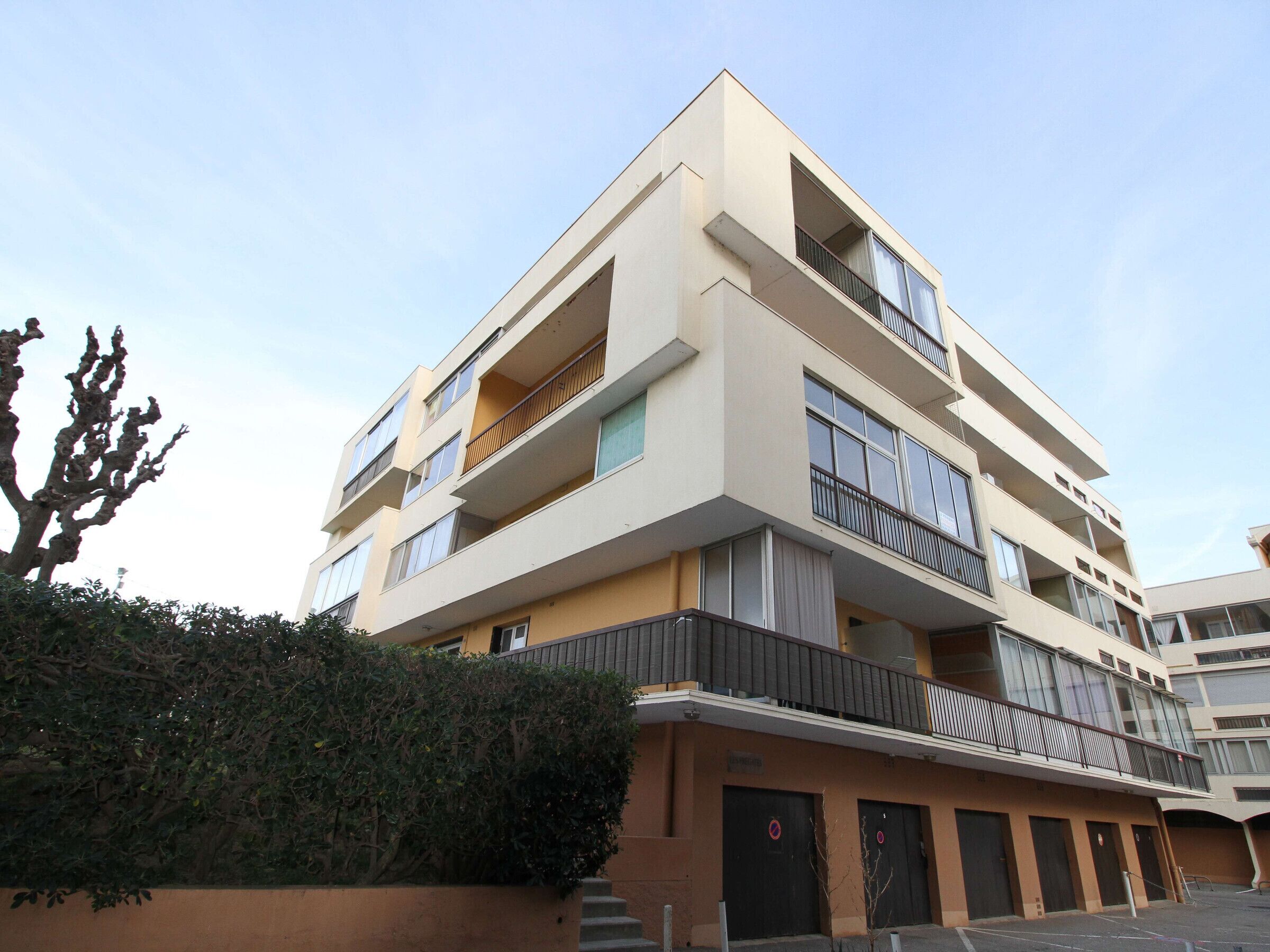 A multi-story residential building with balconies, a flat roof, and a beige facade.