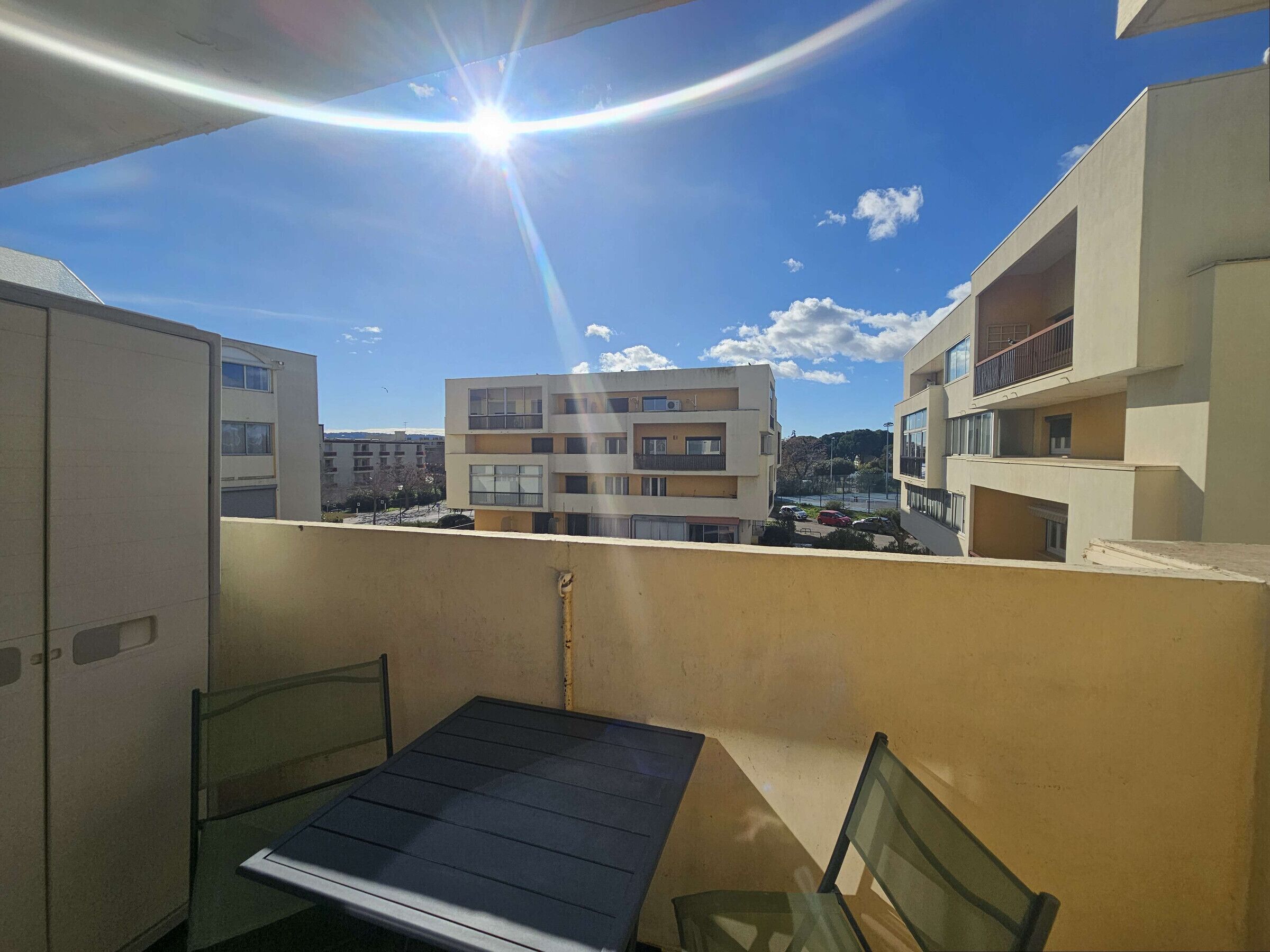 A balcony with a table and chairs, overlooking a residential area with multi-story buildings.
