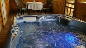 Una cabaña de madera con un jacuzzi en el centro, rodeada por un comedor con sillas y una mesa.