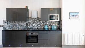 A modern kitchen with dark cabinets, a patterned backsplash, a microwave, a toaster, and a built-in oven. - Brand new luxury apartment with stunning sea views (Aberystwyth)