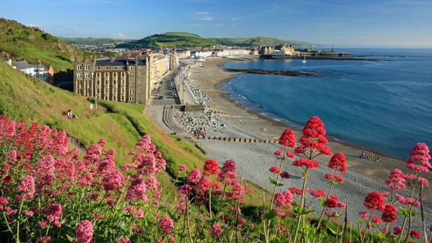 A coastal town with a prominent building, a curved beach, and a rocky shoreline. - Brand new luxury apartment with stunning sea views (Aberystwyth)