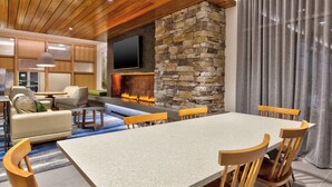 A modern living room with a stone fireplace, a flat-screen TV mounted above it, and a dining area with a large table and wooden chairs. -  Fairfield by Marriott Inn & Suites Knoxville Airport Alcoa (Alcoa)