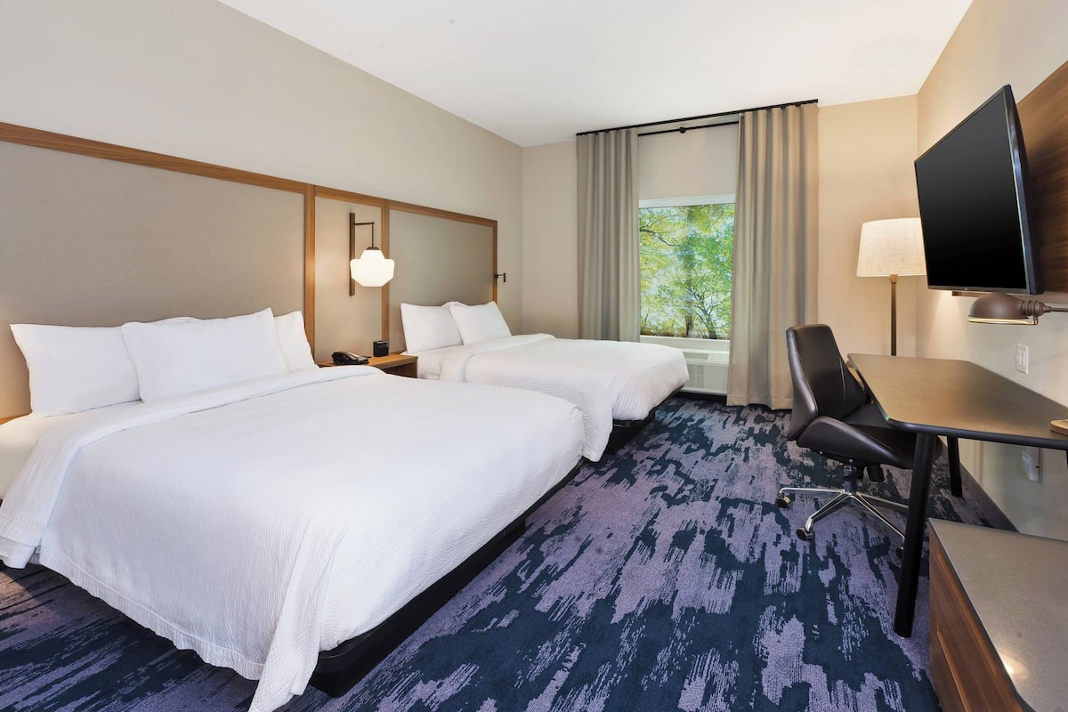 A hotel room with two beds, a desk, a chair, a TV, and a window with curtains.