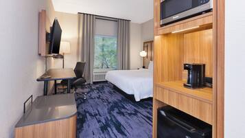 A hotel room with a bed, a desk, a chair, a microwave, a coffee maker, and a refrigerator.