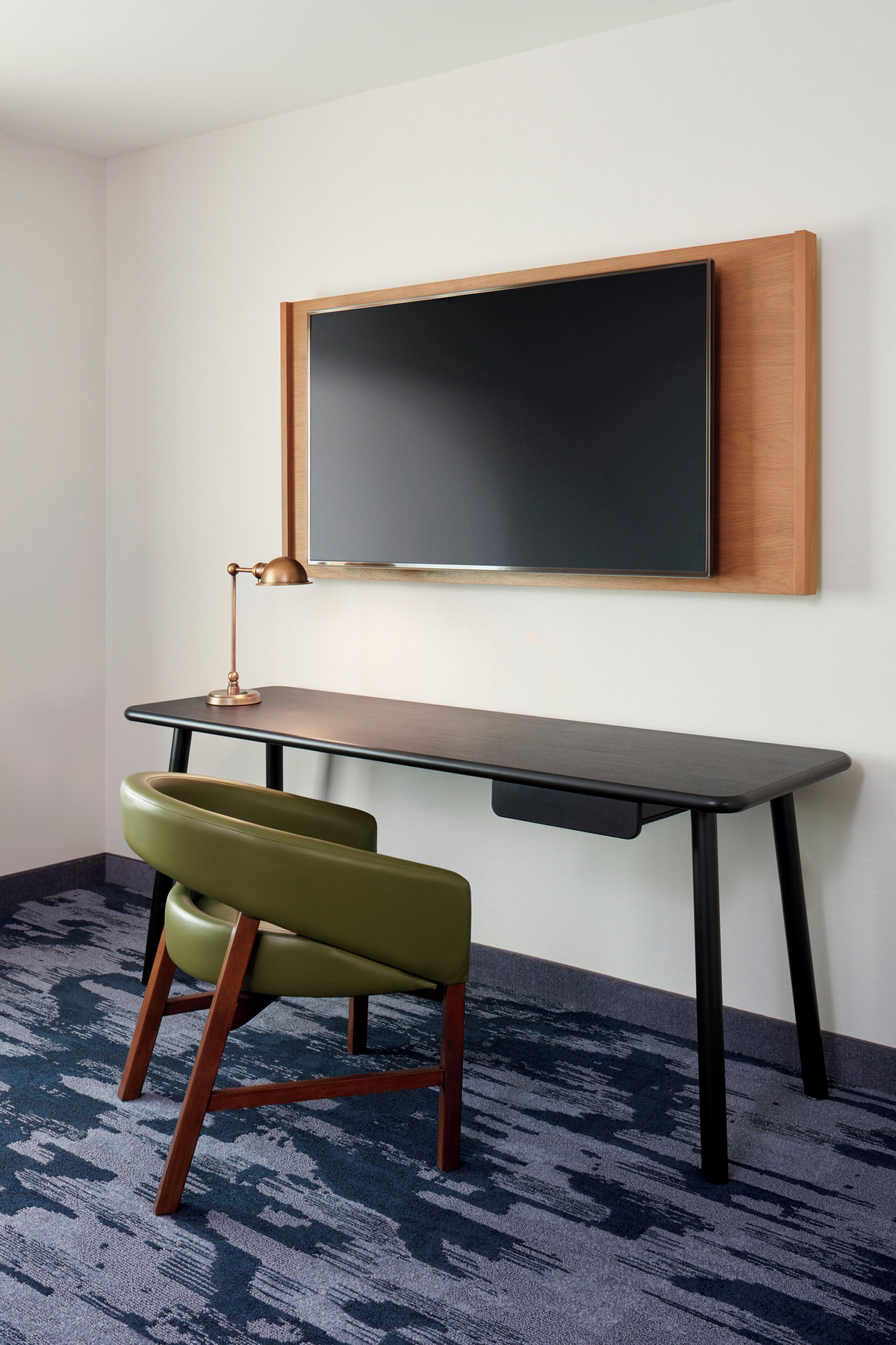 Una habitación con escritorio, silla, televisor de pared y alfombra estampada.