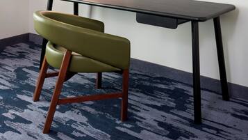 Una habitación con escritorio, silla, televisor de pared y alfombra estampada.