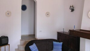 A living room with a sofa, a television on a stand, a fireplace, and a staircase. - Apartment on Costa Rei with Sea View (Costa Rei)