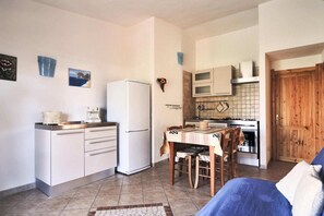 Una cucina compatta con frigorifero, microonde e fornello. Nell'area soggiorno, un tavolo da pranzo con sedie e un divano blu.