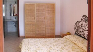 A bedroom with a bed, a wardrobe, and a bathroom visible through an open door. - Apartment on Costa Rei with Sea View (Costa Rei)