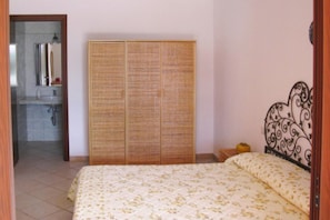 Una camera da letto con un letto, un armadio e un bagno visibile attraverso una porta aperta.