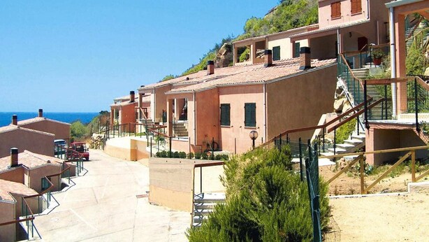 A coastal residential area with terraced houses, a clear sky, and a view of the sea. - Apartment on Costa Rei with Sea View (Costa Rei)