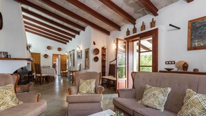 A spacious living room with a high ceiling and exposed wooden beams, furnished with sofas and armchairs, a coffee table, and decorative items. - Finca Sa Bastida (Sant Joan)