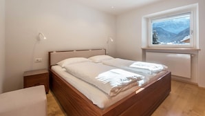 Een slaapkamer met een houten bed, een nachtkastje, een raam met uitzicht op bergen en inbouwspots.