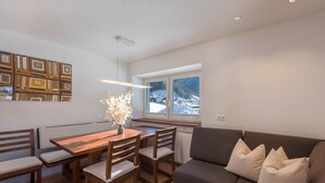 Een moderne woonruimte met een eethoek, een bank en uitzicht op een besneeerd landschap.