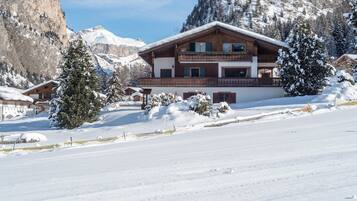 Een hotel in chaletstijl met een houten gevel, meerdere balkons en een besneeerd landschap met bergen op de achtergrond.